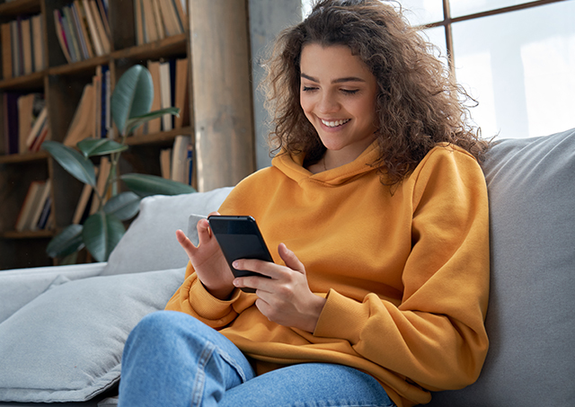 Smiling young woman relaxing on a sofa while using her mobile phone